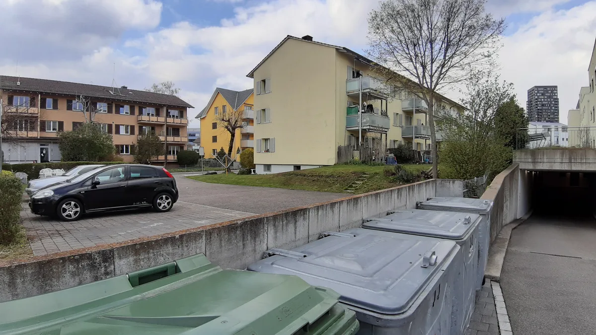 Hier im Birchlen-Quartier gibt es noch günstigen Wohnraum, doch das Gebiet soll verdichtet werden. Block, Container, ein Parkplatz und mehrere alte Wohngebäude.